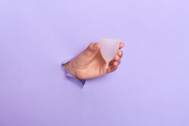 Photo close up shot of human's hand holding menstrual cup in hole of purple paper wall modern sanitary products for period women health gynecology hygiene zero waste alternatives