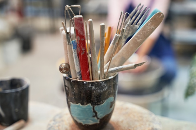 Close up shot of jar with tools, brushes for creating handmade clay ceramics in workshop studio 