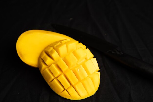 Close up shot of juicy sweet mango cut next to a black knife on a black cloth