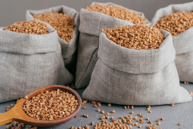 Close up shot of little sack made of linen fabric filled with dry brown buckwheat wooden spoon with raw cereal Selective focus