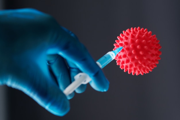 Close-up shot. Male doctor holds syringe with injection Syringe and red coronavirus. Covid-19 Pandemic Coronavirus.