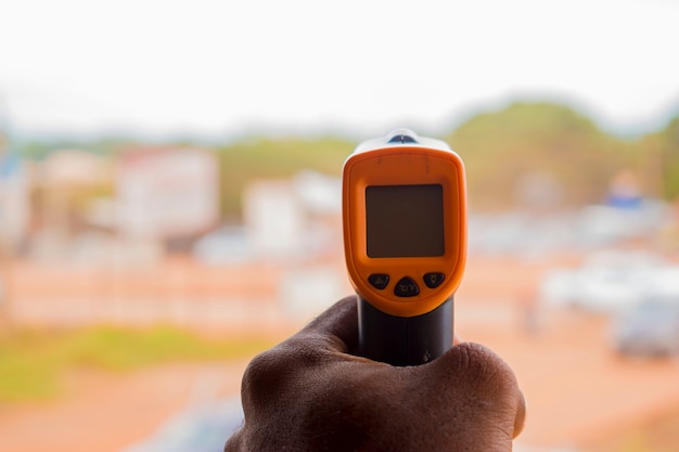 Foto primo piano di un uomo pronto per l'uso del termometro frontale a infrarossi (pistola termometro) per controllare la temperatura corporea per i sintomi del virus - concetto di epidemia di virus epidemico