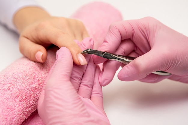 Close-up shot of a manicurist using a cuticle clipper to give a nail manicure to her client in the beauty salon. Master of manicure remove a cuticle nail with nail clipper.