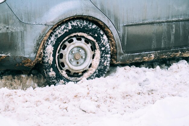 Close up shot of an old green car tire full of dirty and white snow in winter