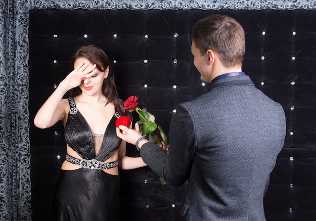 Close up Shot of Overwhelmed Young Woman in Elegant Black Dress Received a Red Rose and Red Jewelry Box from her Happy Boyfriend