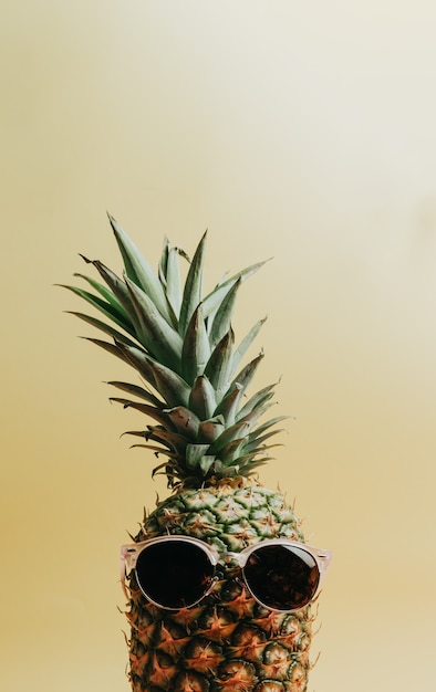 Immagine ravvicinata di un ananas con un paio di occhiali da sole su uno sfondo giallo pastello, spazio copia, concetto di estate e vacanza