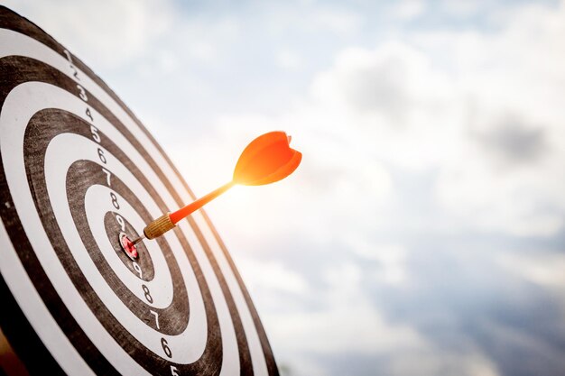 Close up shot red darts arrows in the target of dartboard
center on dark blue sky background. business target or goal success
and winner concept.