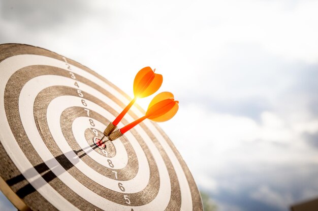 Close up shot red darts arrows in the target of dartboard
center on dark blue sky background. business target or goal success
and winner concept.