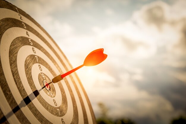 Close up shot red darts arrows in the target of dartboard
center on dark blue sky background. business target or goal success
and winner concept.