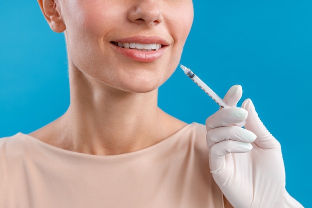 Close up shot of smiling woman receiving botox injection in lips from beautician