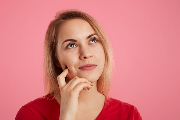 Close up shot of thoughtful dreamy young beautiful female looks pensively upwards