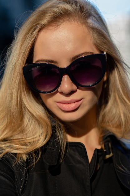 Close-up shot van aantrekkelijke vrouw met natuurlijke make-up die zwarte trenchcoat en bril draagt