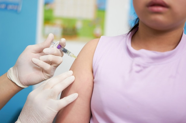 Close-up shot van arts die vaccininjectie gebruikt voor covid-immunisatie op de schouder van een Aziatisch kind met angstangst