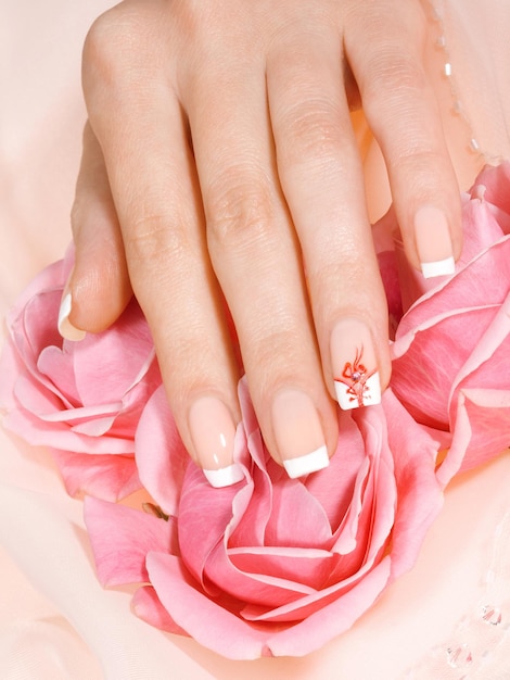 Foto close-up shot van de hand van de vrouw met french manicure op roze bloemen xabackgroundxa