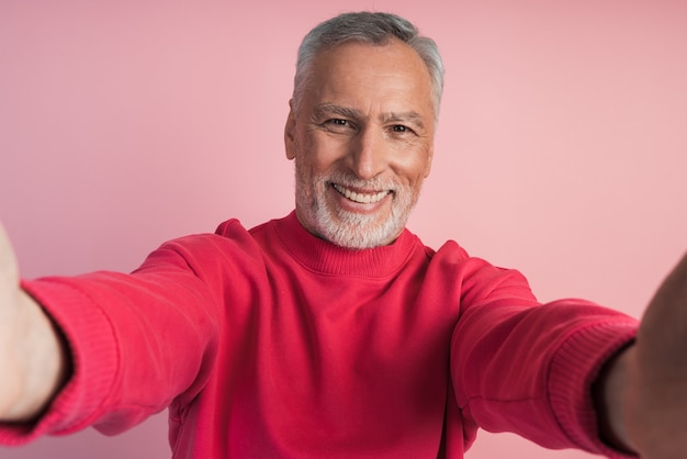 Close-up shot van de handen van een senior man die zijn telefoon vasthoudt, een selfie neemt op een roze muur