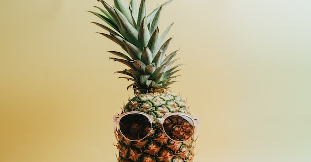 Close-up shot van een ananas met een zonnebril op een pastelgele achtergrond, kopieerruimte, zomer- en vakantieconcept