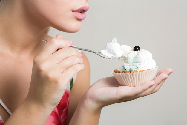 Close-up shot van een jong blond model dat een smakelijk zoet dessert met botercrème eet