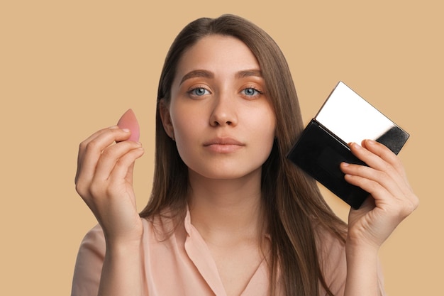 Close-up shot van een jonge vrouw met een make-up blender spons en een spiegel