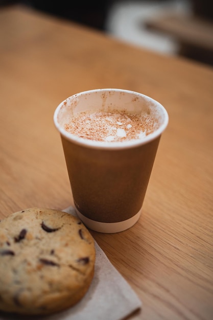 Close-up shot van een kop hete cappuccino met een chocoladekoekje ernaast in een cafetaria