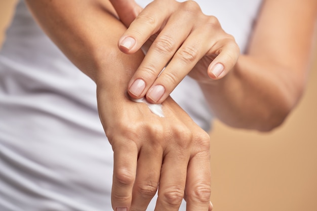 Close-up shot van een vrouw die vochtinbrengende handcrème gebruikt terwijl ze tegen een beige achtergrond staat