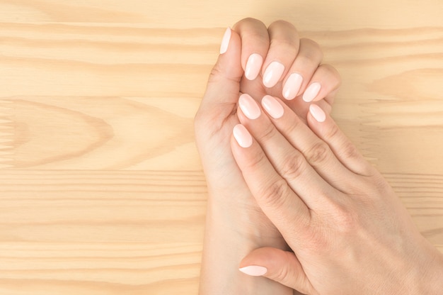 Foto close-up shot van een vrouw in een nagelsalon die een manicure krijgt. houten achtergrond. mooie verzorgde vrouwenhanden met witroze nagels