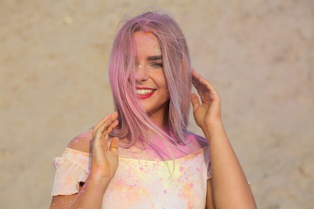 Close-up shot van expressief blond model met rode lippenstift bedekt met roze droge verf Holi in de woestijn