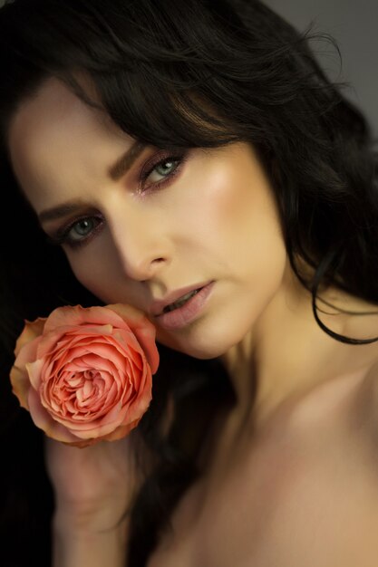 Close-up shot van het gezicht van een mooie vrouw met een oranje roos. Vrouw met luxe make-up en perfecte huid