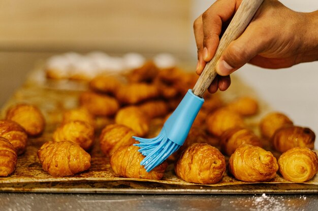 Close-up shot van kleine croissants vers gebakken met een mannenhand insmeren met zoete siroop