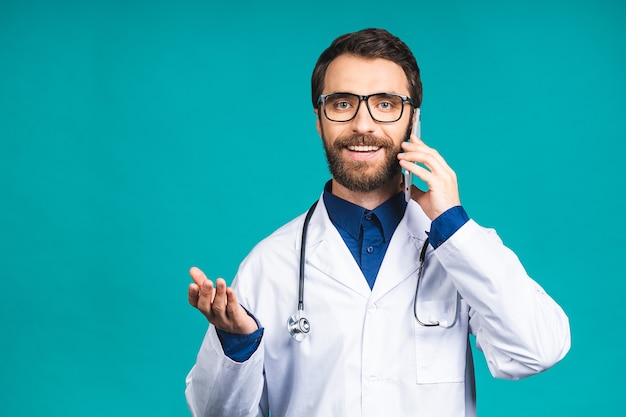 Close-up shot van knappe jonge man arts geïsoleerd op blauwe achtergrond praten op smartphone, positief glimlachend. Mobiele telefoon gebruiken.