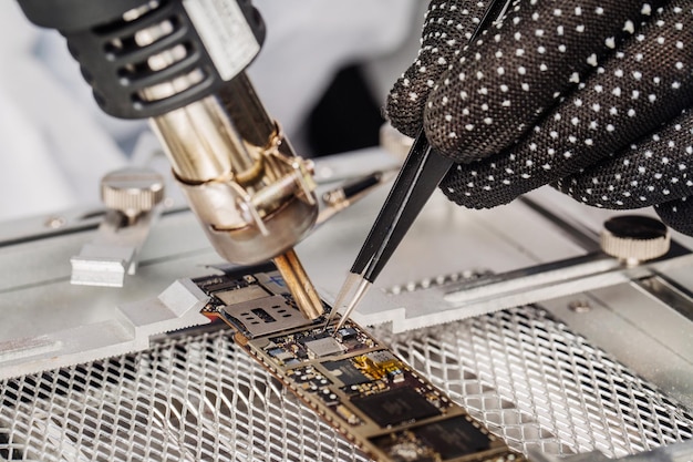 Close-up shot van mannelijke handen werken met soldeerbout op het demonteren van printplaat in mobiel telefoonapparaat