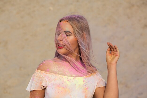 Close-up shot van schattig blond model met rode lippenstift bedekt met roze droge verf Holi in de woestijn