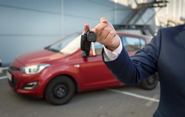 Close-up shot van verkoopmanager die autosleutels vasthoudt tegen nieuwe auto