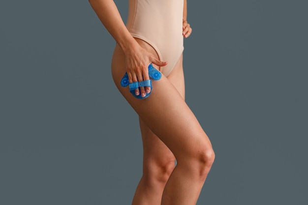 Крупным планом снимок женщины в бежевом боди, массирующей бедро массажной перчаткой в форме ладони