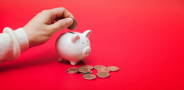 Close up shot of woman hand putting money coin into piggy