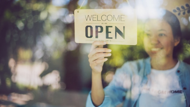 Photo close up shot of woman hand turning open sign board on glass door in coffee shop and restaurant.