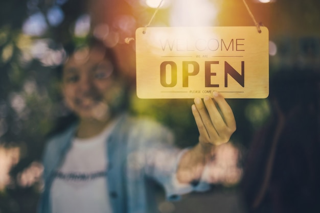 Photo close up shot of woman hand turning open sign board on glass door in coffee shop and restaurant.