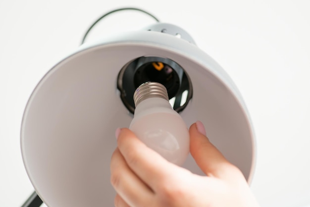 Close up shot of woman's hand changes a light bulb in grey lamp