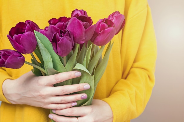 Close-up shot of woman in yellow sweater holding a bouquet of purple tulips