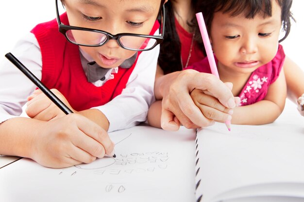 Photo close-up of siblings writing in book at home