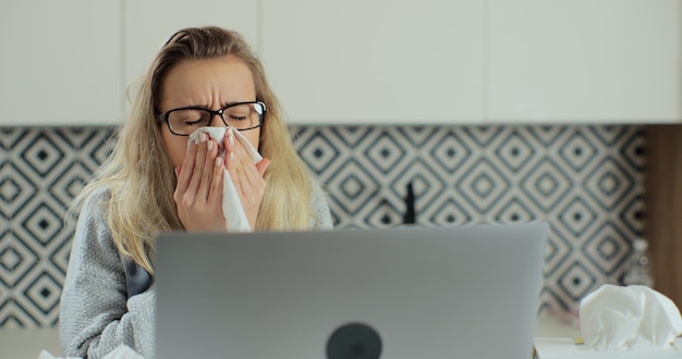 Photo close up of sick woman blows her nose into a paper napkin while working remotely at home. concept of healthcare and illness.