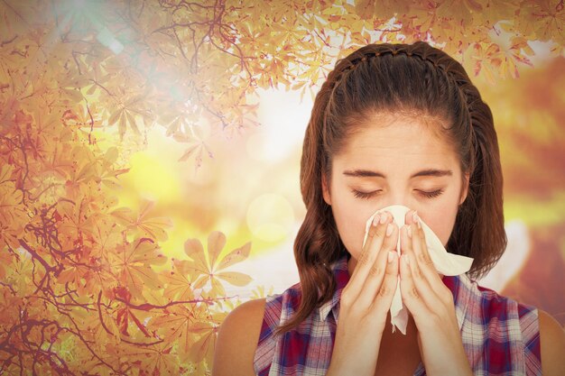 Close-up of sick woman sneezing in a tissue against autumn scene