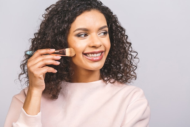 Close up side portrait of beautiful aro american woman applying makeup with brush