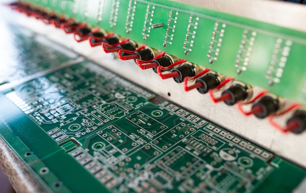 Close-up side view of complex microcircuits and green boards on a panel connected to each other using red wires in the production of military equipment. Secret Technology Concept