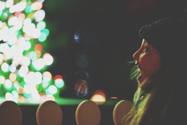 Foto vista laterale da vicino di una ragazza che urla mentre guarda via in una città illuminata di notte durante il natale