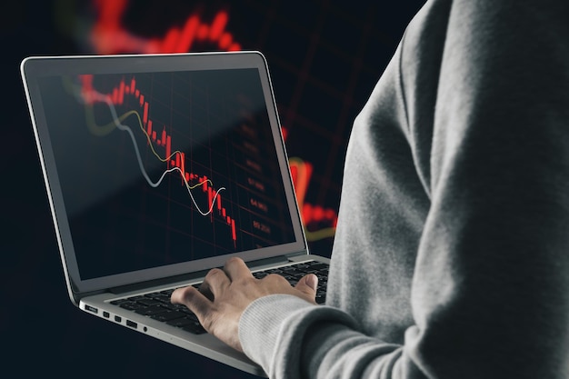 Close up and side view of hand using laptop with abstract falling red forex chart on dark background Economic decline and loss concept