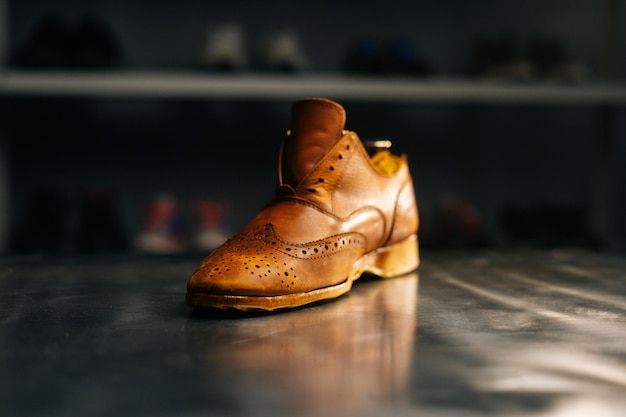 Close-up side view of old light brown leather shoes with wooden shoe pad to be repaired in dark craft shoe shop. Concept of cobbler artisan repairing and restoration work in shoe repair shop.