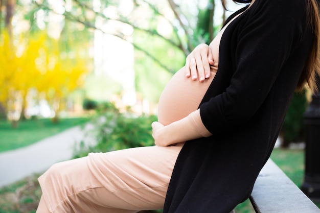 Крупным планом фото молодой беременной женщины, сидящей на скамейке, отдыхающей и расслабляющейся