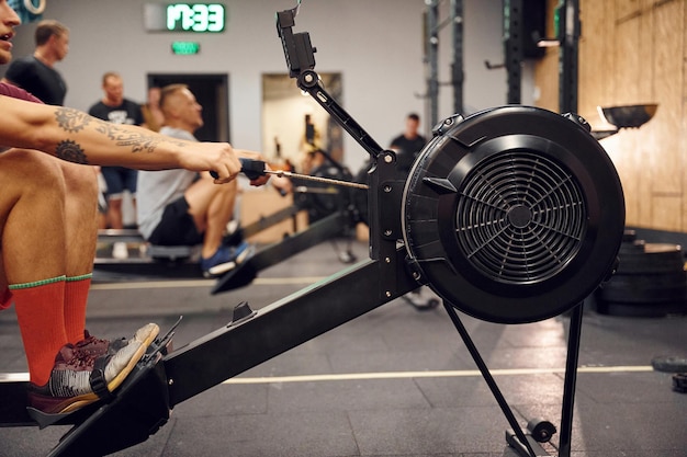 Close up side view Sportive man doing exercises on rowing machine in the gym