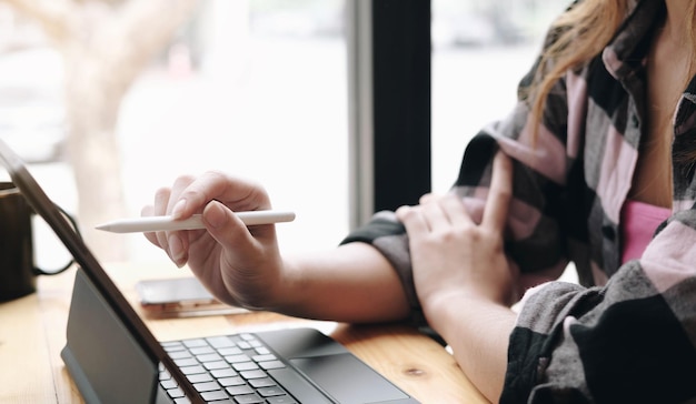 Photo close up side view women sitting at table woman holding stylus pen and point to digital tablet