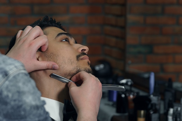 Close-up side view of young bearded man getting beard haircut by hairdresser at barbershop.